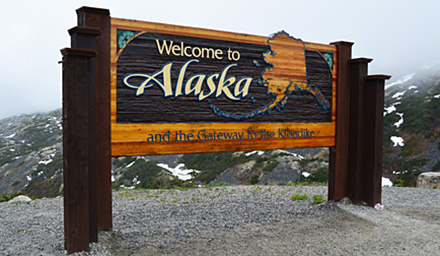Welcome to Alaska wooden sign against snow capped rocky mountains