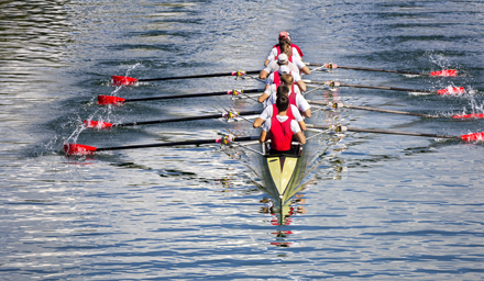 A rowing team of 8 people wearing red vests and red paddles