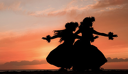 Silhouette of two women performing the hula against an orange sunset in Hawaii