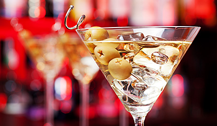 A martini cocktail with olives with a red background