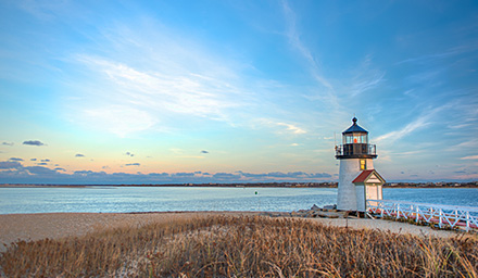 Lighthouse lining the water with a sunrise in the background against a blue sky