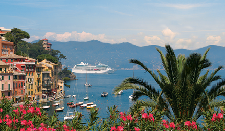 Oceania Cruises ship in the distance with colored houses and palm trees and pink flowers